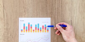 person holding a blue pen while pointing at paper with graphs